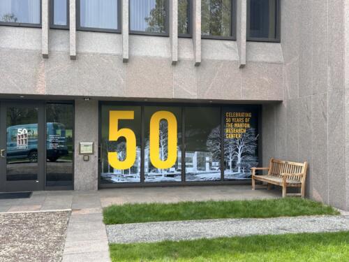 Large window graphics announcing museum's 50th anniversary. Yellow lettering with white ghosted rendering of campus building