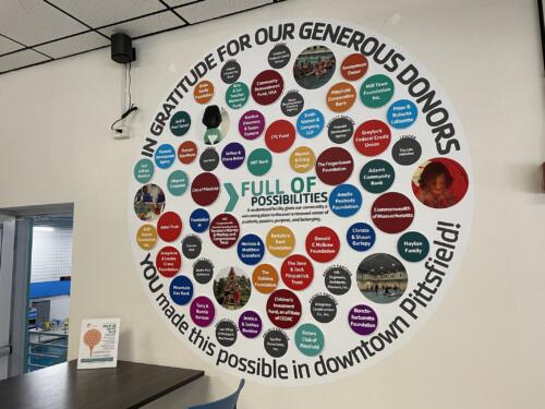 Colorful circular donor wall display for nonprofit organization. Raised PVC circles feature individual donor names and photos