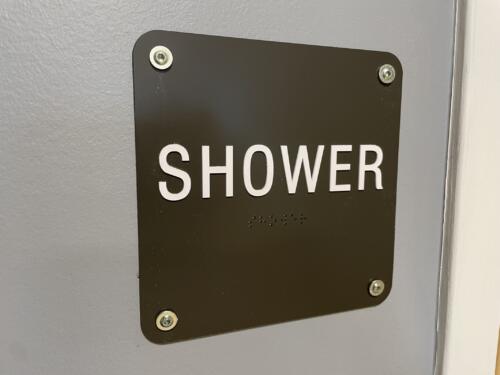 Interior hospital sign reads "shower" with braille. ADA complient wayfinding.