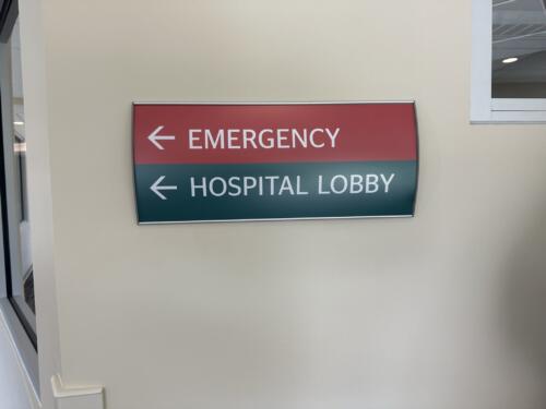 Interior wayfinding sign for hospital. Sign reads "emergency and hospital lobby" with directional arrows.