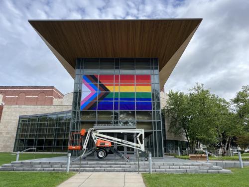 Panels of the window come together to form the Progress Pride flag.